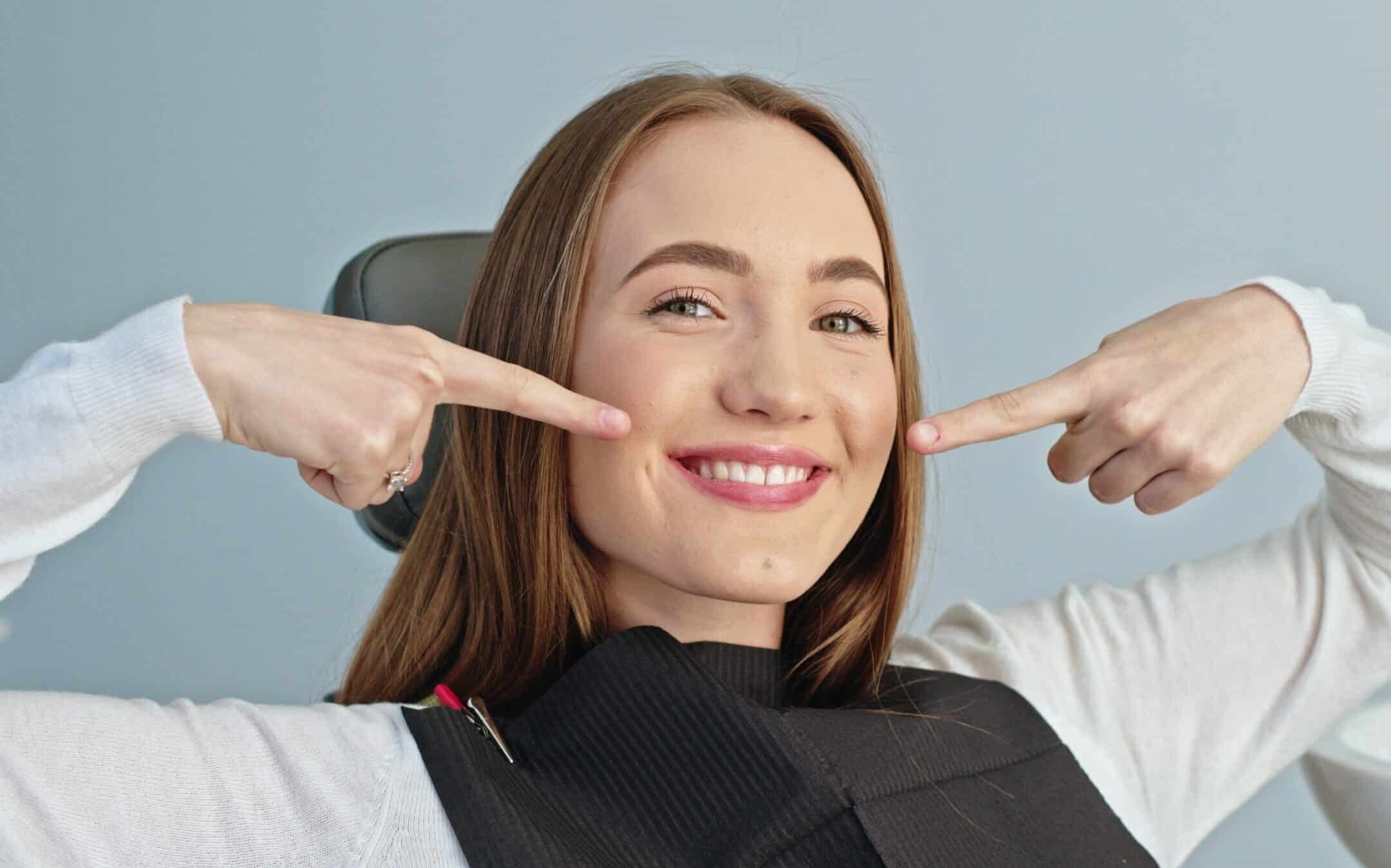 Showcasing,A,Flawless,Smile:,Young,Woman,Pointing,At,Her,White